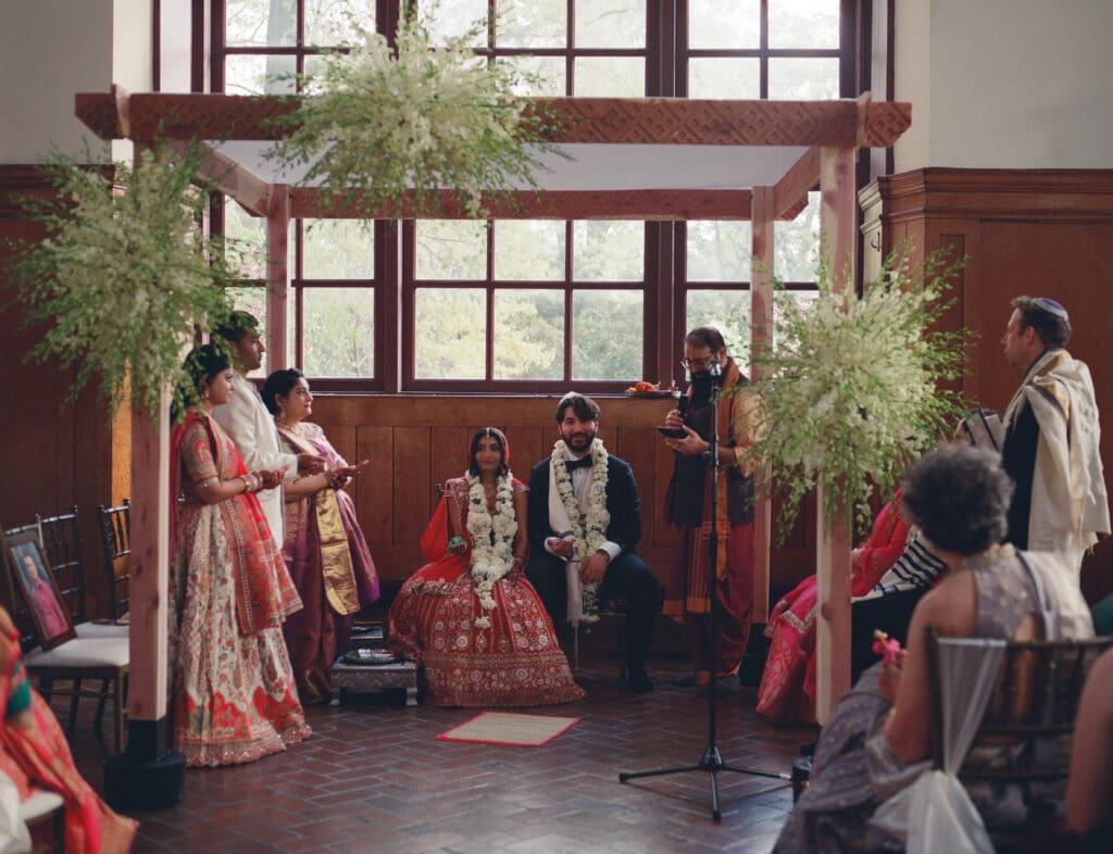 Bride and groom sitting at the altar surrounded by family during a Hindu Jewish wedding