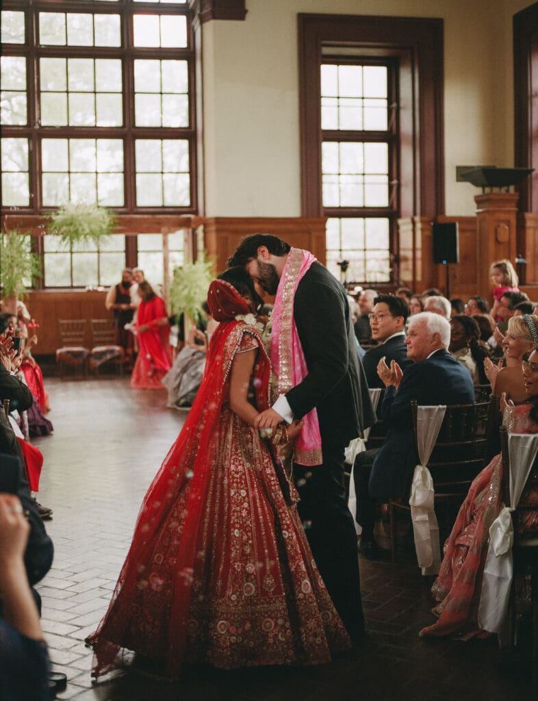 Bride and groom kissing at the end of the aisle at a Hindu Jewish wedding ceremony