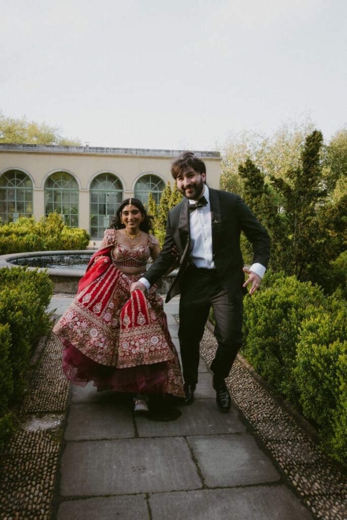 Bride and groom running through a garden holding hands