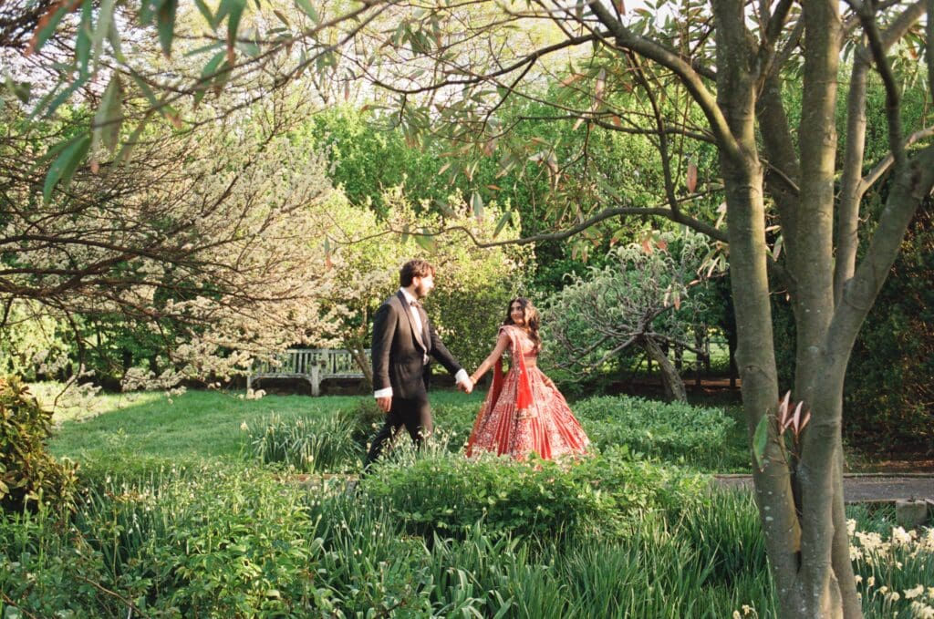Bride leading the groom through a walk in a garden