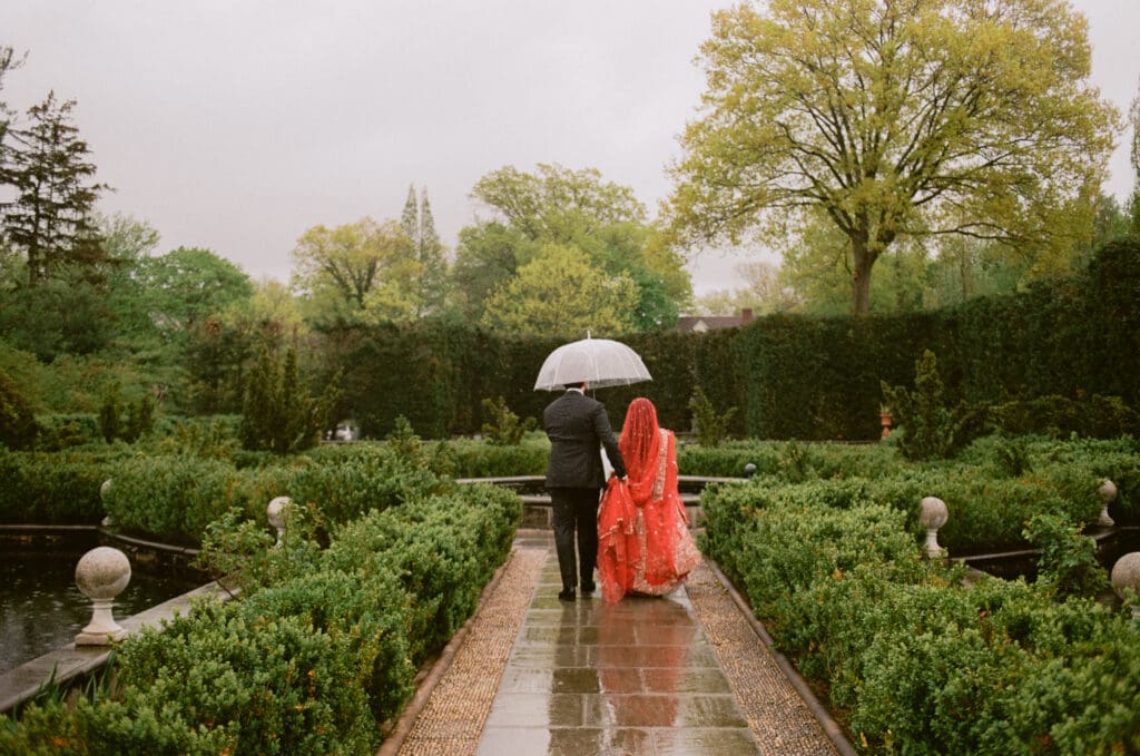 Bride and groom walking through a garden with an umbrella