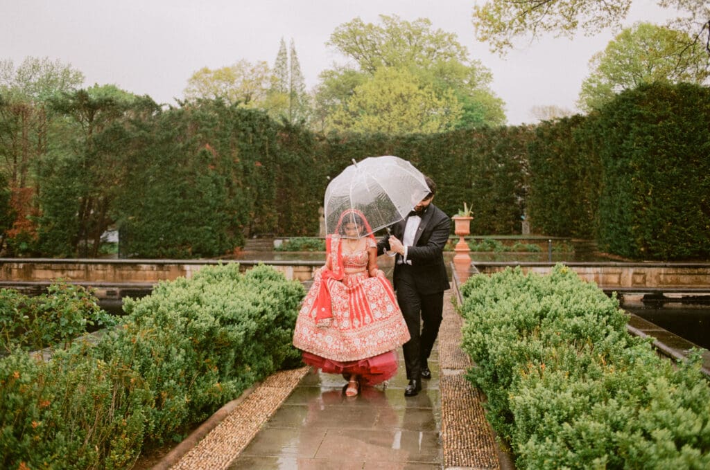 Bride and groom running through a garden under an umbrella