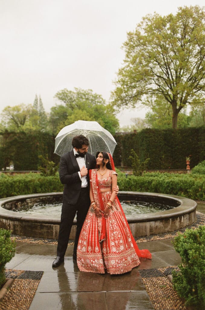 Bride and groom standing in a garden looking at each other with an umbrella 