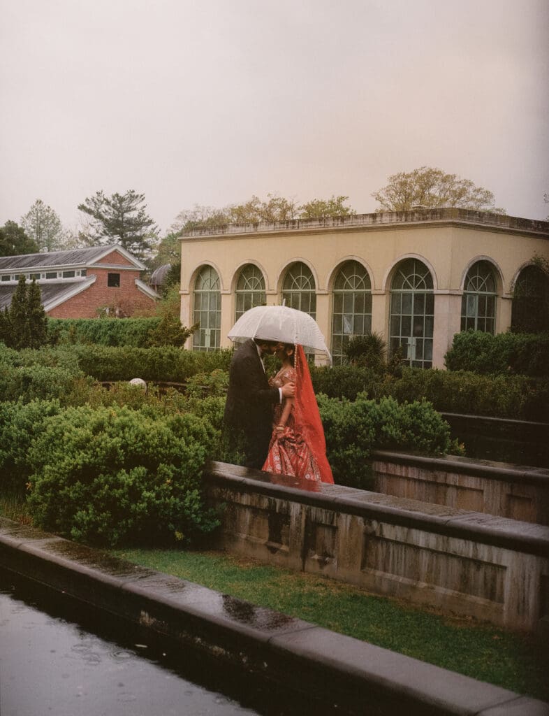 Bride and groom kissing under an umbrella in a garden