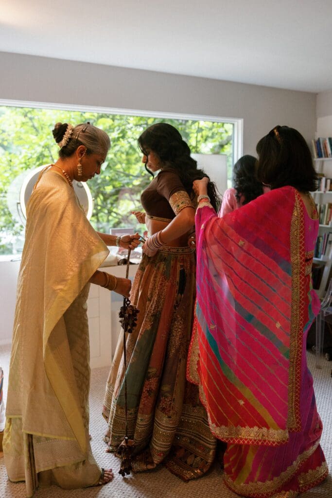 Bride getting dressed in her lehenga with help of her family members