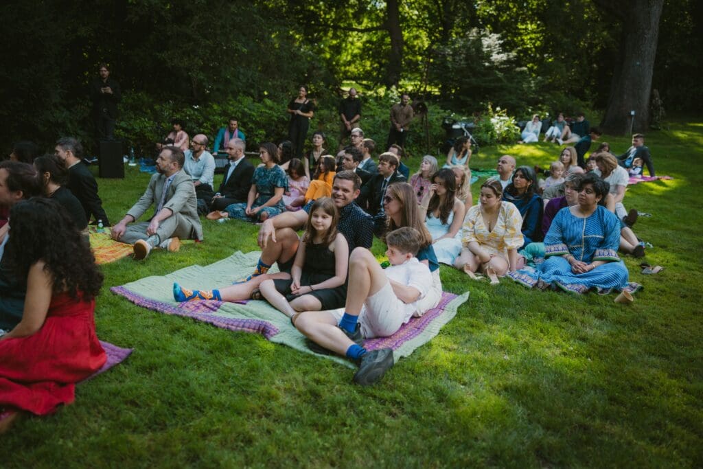 Wedding guests sitting on blankets in the grass at a whimsical backyard wedding ceremony