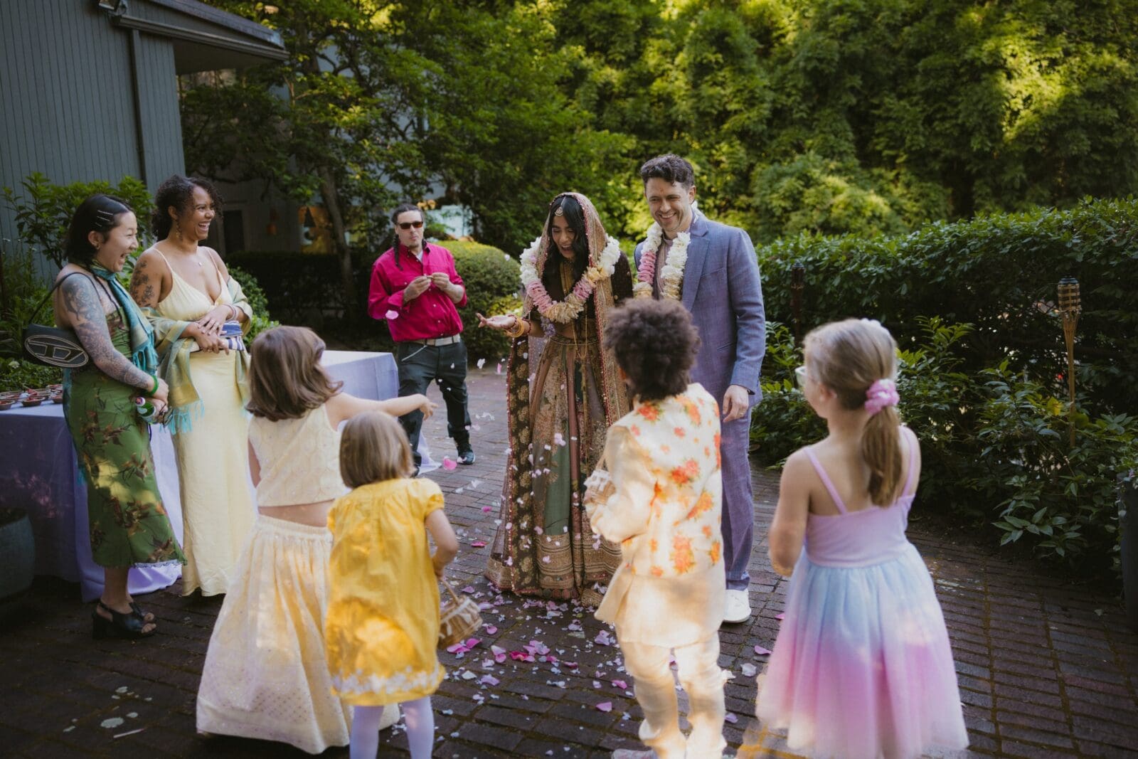 Bride and groom laughing while children throw flower petals on them