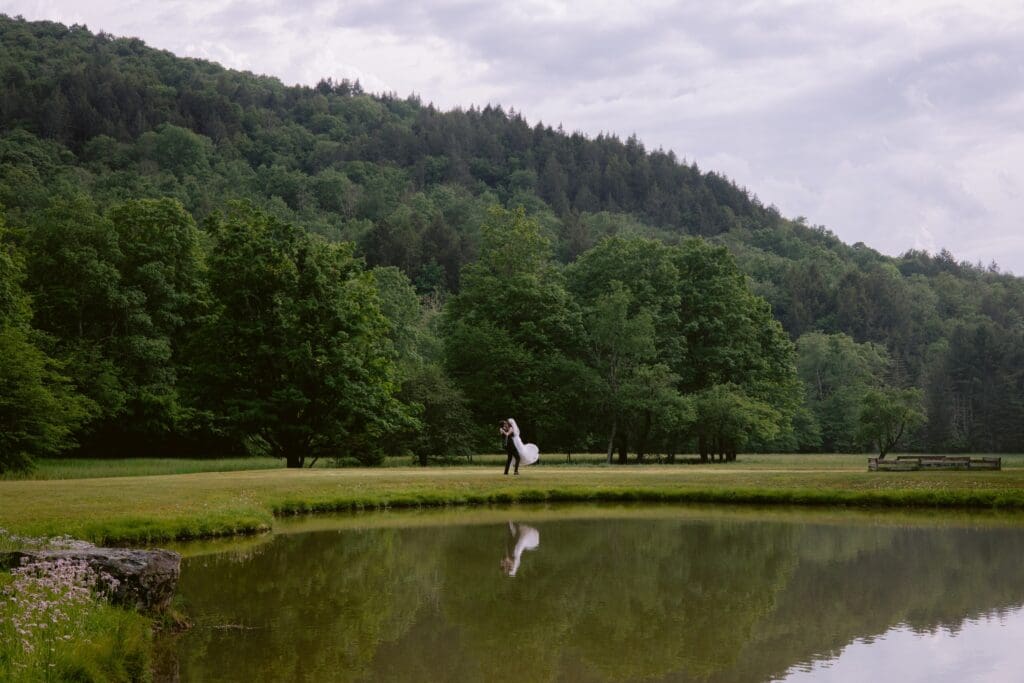 Bride jumping into the groom's arms from across a pond with mountains in the background