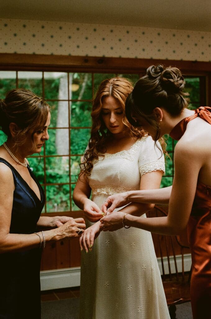 Bride putting on jewelry with the help of her mother and sister