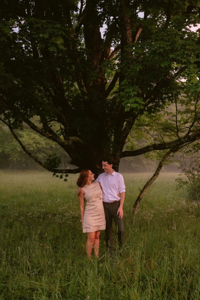 Bride and groom looking at each other standing in tall grass in front of a tree at sunset