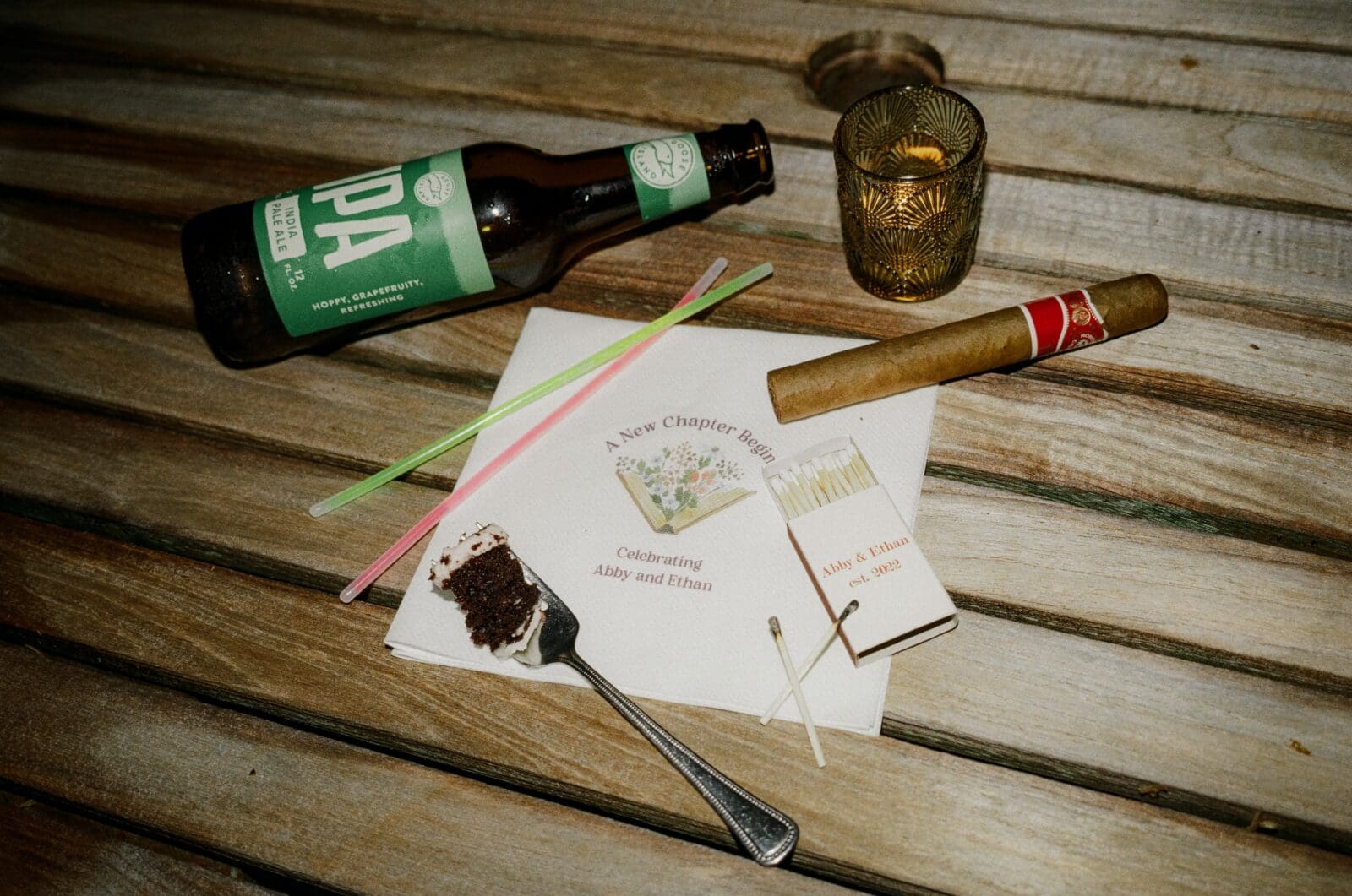 Late night flatlay with a beer bottle, cigar, glow sticks, matchbox, and fork of cake