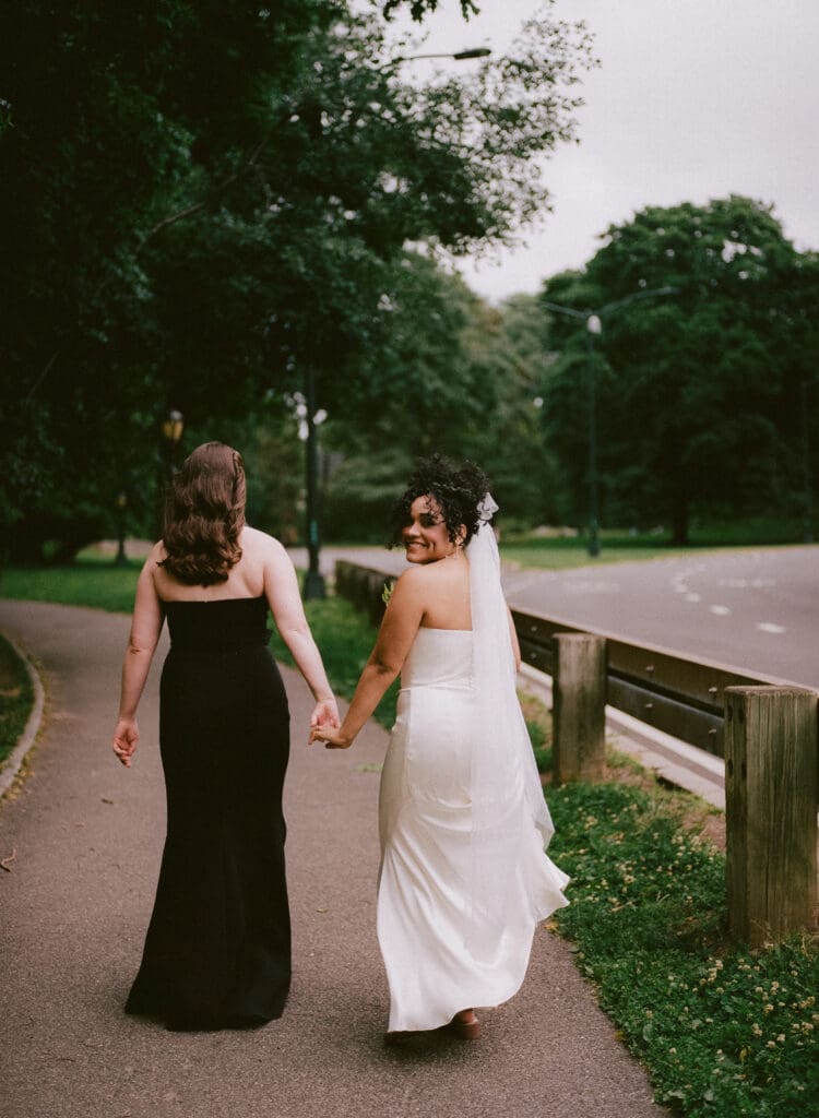 Brides walking in Central Park, taken from behind with one bride looking back at the camera 