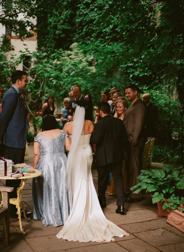 Bride walking down the aisle with her mom and brother at a New York City garden wedding, taken from behind