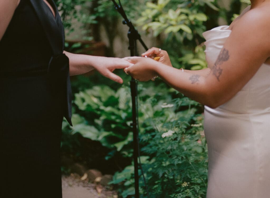 Bride placing the ring on the other bride's finger at a New York City garden wedding