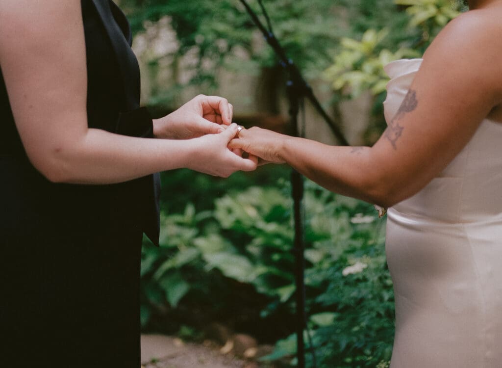 Bride placing the ring on the other bride's finger at a New York City garden wedding