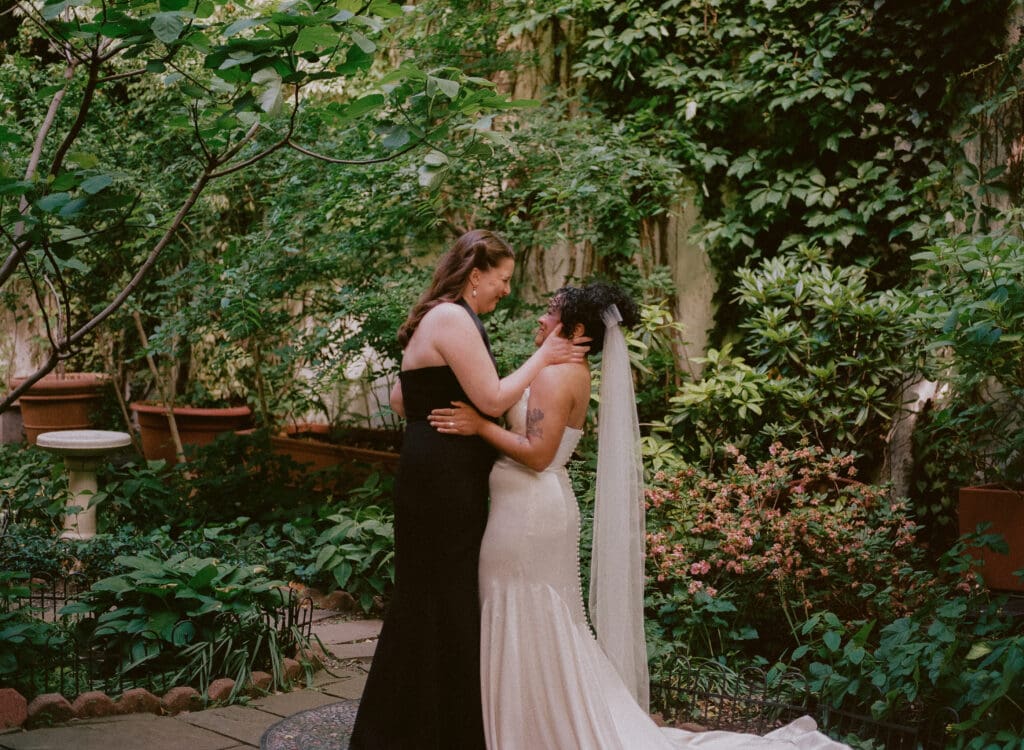 Brides smiling and holding each other at the altar during a New York City garden wedding