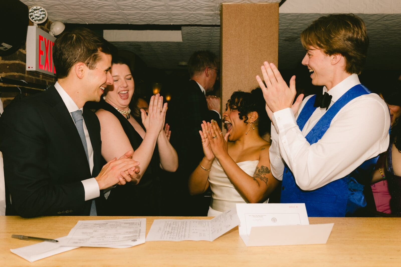 Brides and witnesses laughing and clapping after signing the wedding license