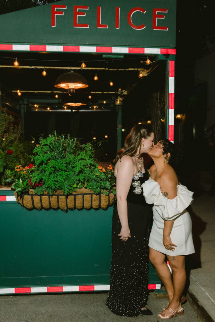 Brides kissing under the wedding reception sign in their second looks