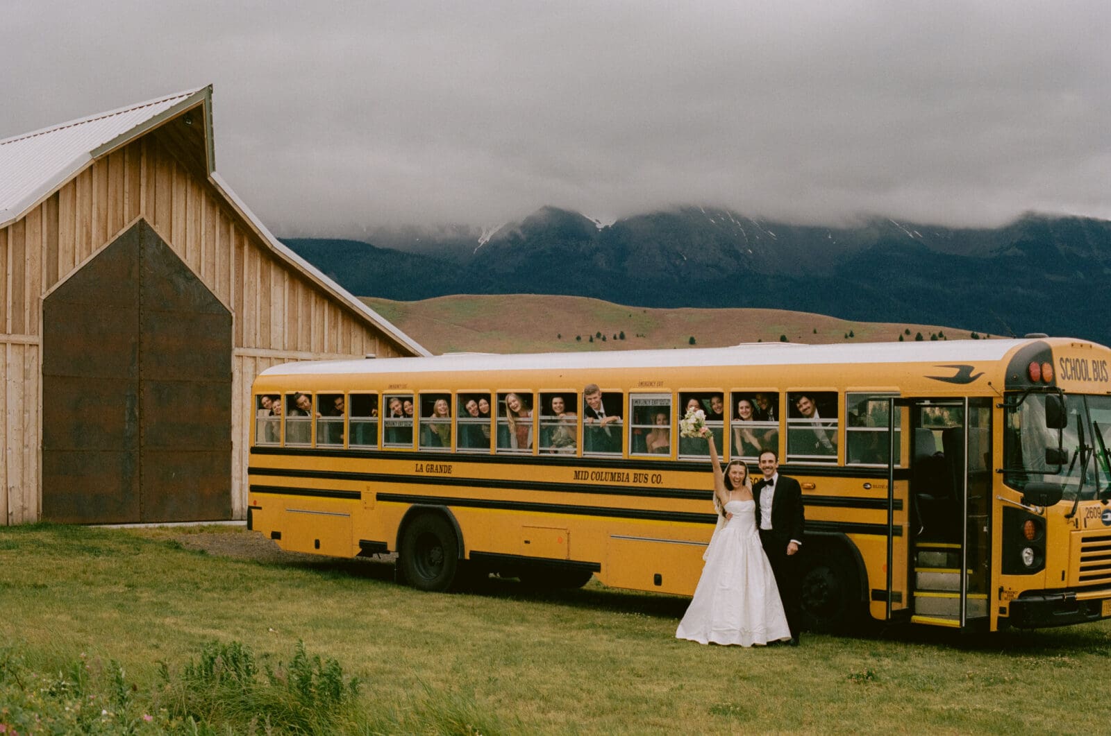 Bride and groom standing in front of a school bus full of their guests