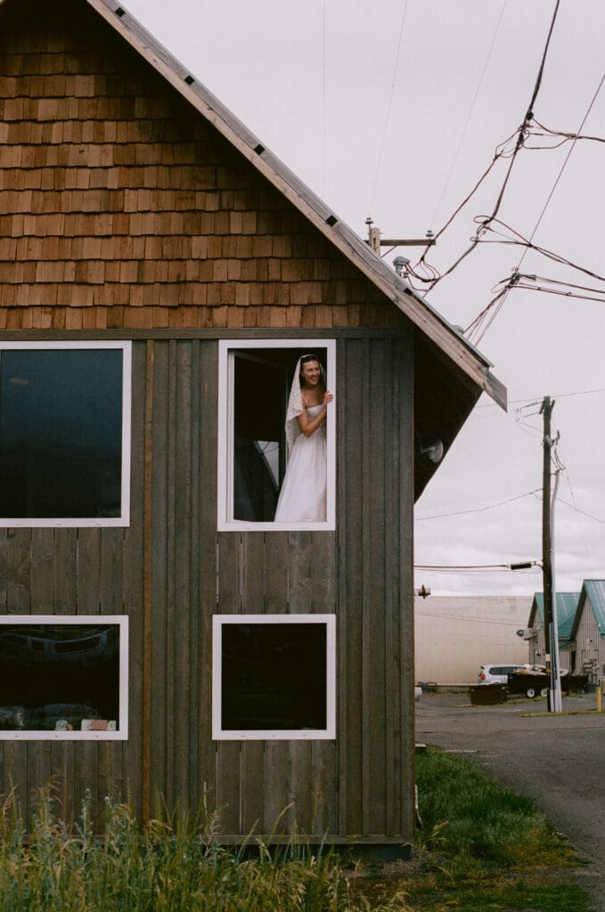Bride looking out the window of a wooden cabin