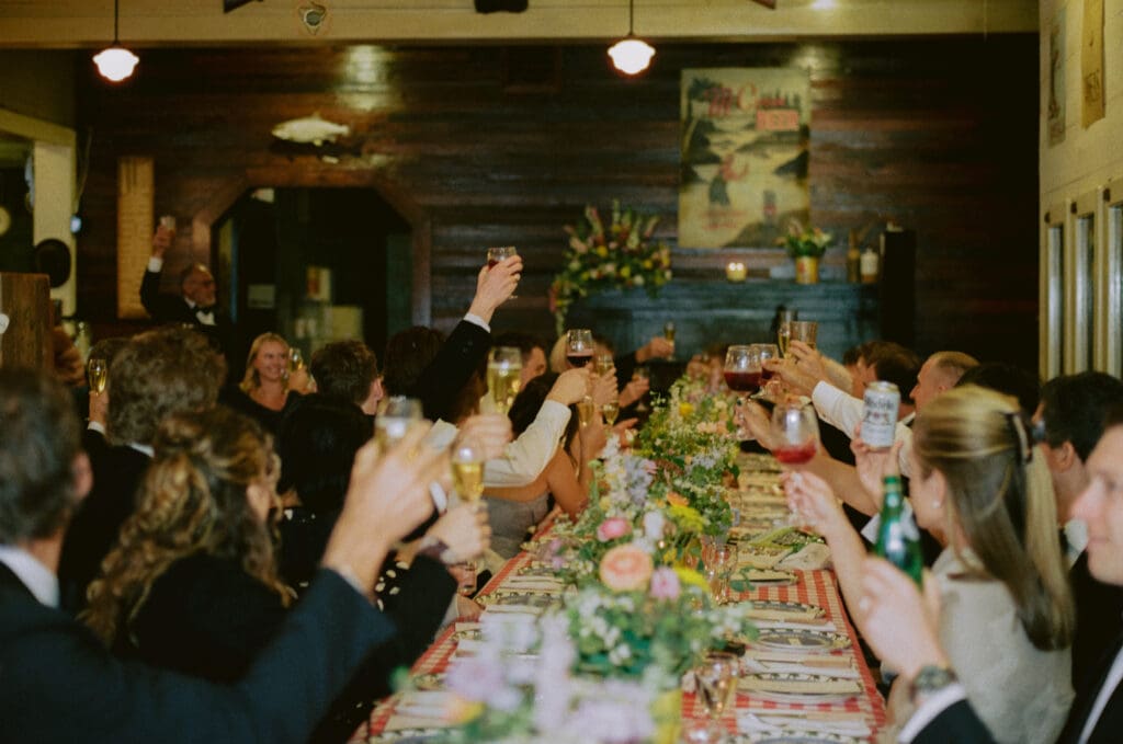 Wedding guests raising their glasses for a toast at a long dinner table