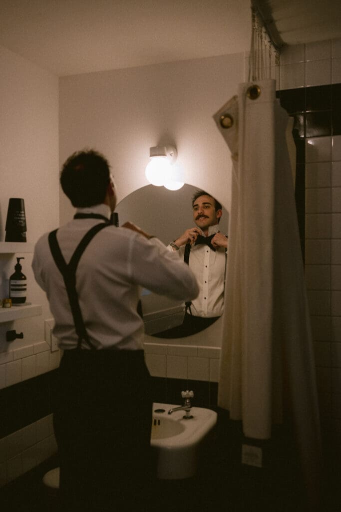 Groom fixing his bowtie in the mirror
