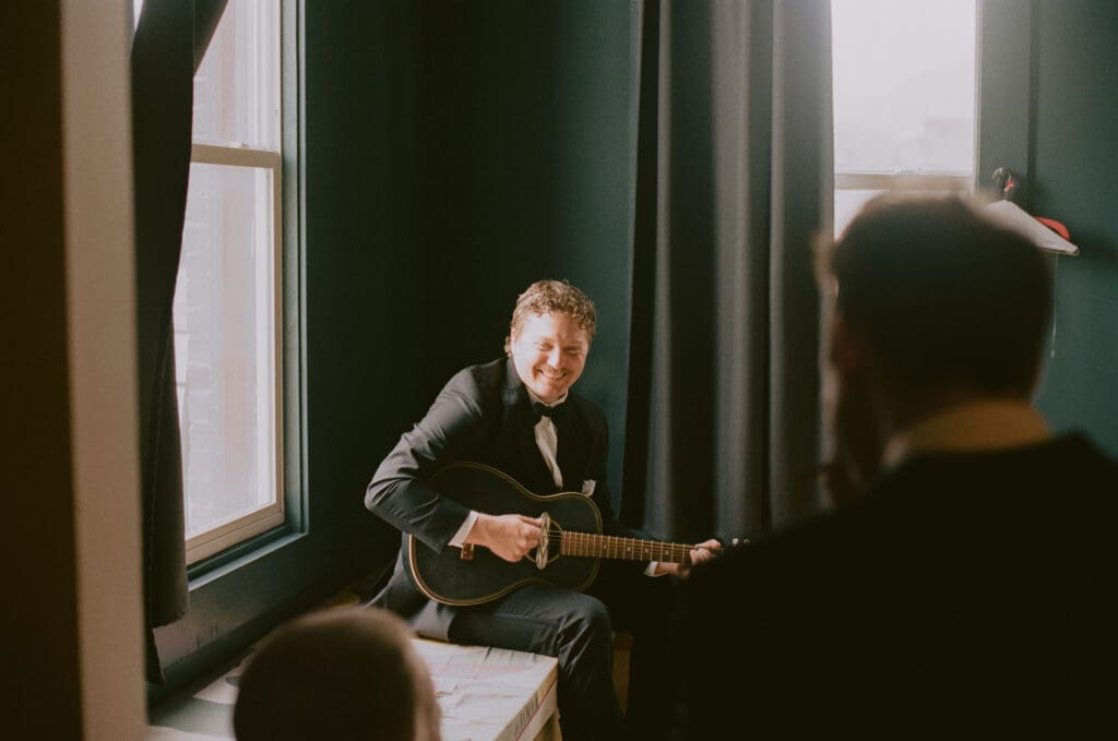 Candid photo of a groomsman playing guitar during getting ready