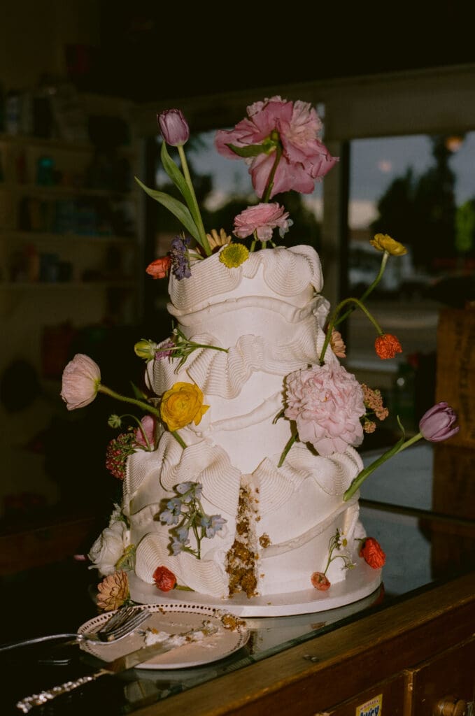 Three tiered wedding cake covered in flowers with a slice cut out