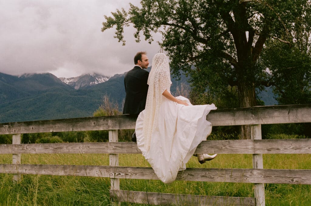 Bride and groom sitting on a fence in a field