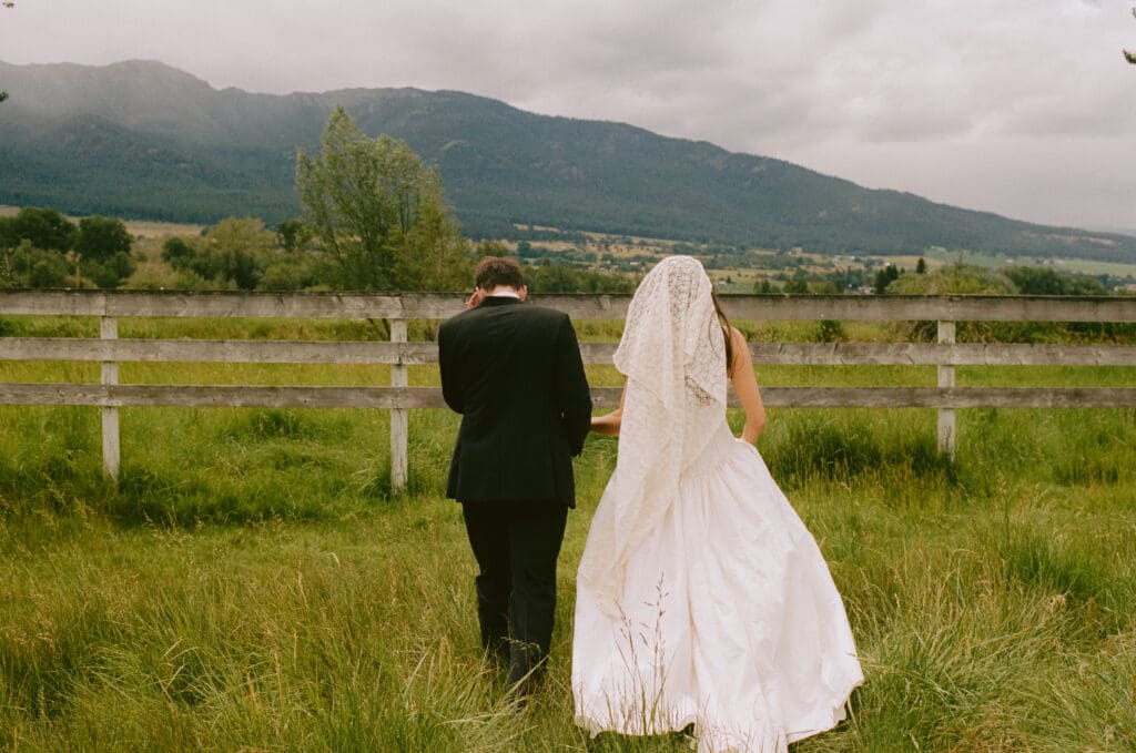 Bride and groom walking in a field, taken from behind