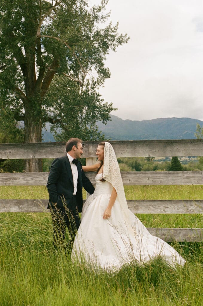 Bride and groom leaning against a fence in a field